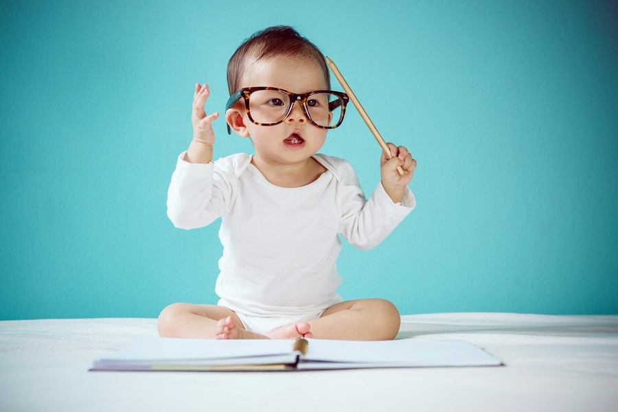 Slimme aziatische baby met bril, potlood en boek