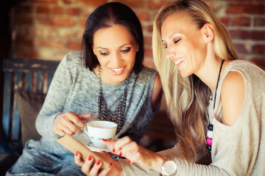 Twee-jonge-vrouwen-in-cafe-drinken-koffie-en-lachen