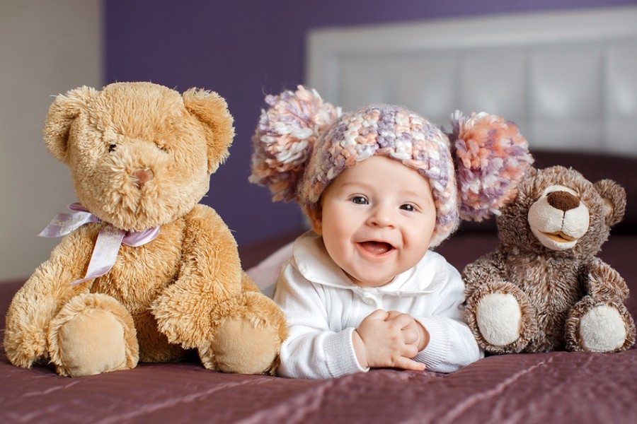 Lachende baby van 25 weken oud zit tussen twee knuffels in