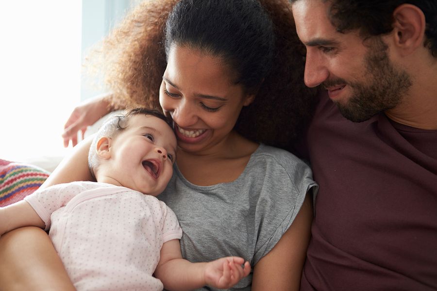 Lachende baby van 26 weken oud zit bij papa en mama
