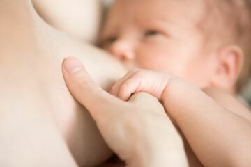 Close up van moeder die borstvoeding geeft aan baby terwijl baby haar hand vasthoudt