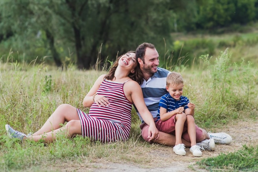 Zwangere vrouw zit lachend samen met gezin op grasveld