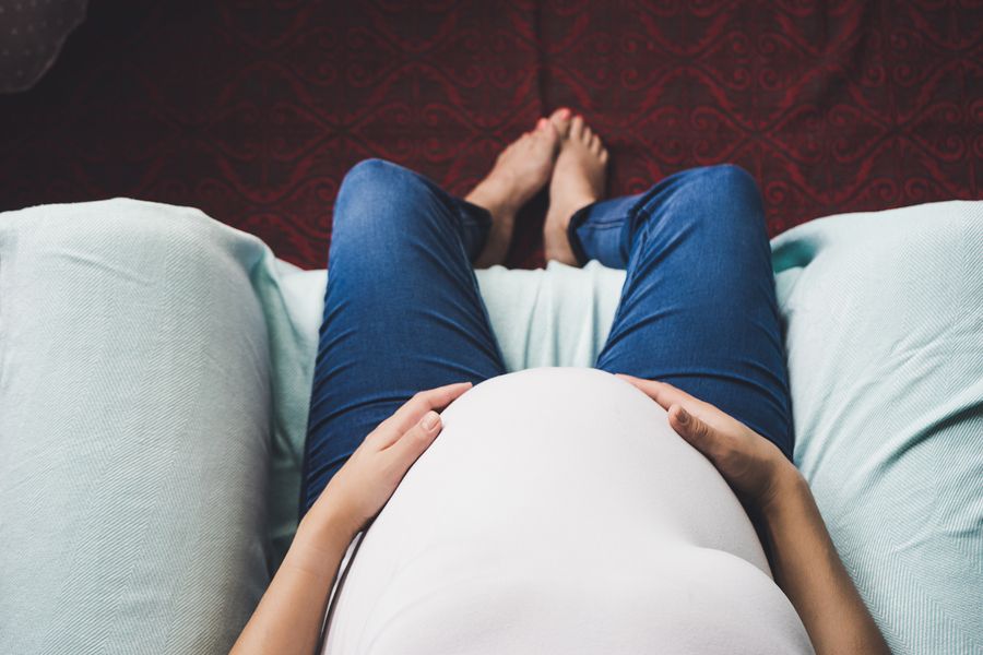 De buik van 24 weken zwangere vrouw zit in de weg bank en houd haar buik vast