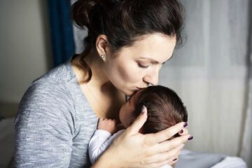 Baby heeft last van regeldagen en moeder kust baby liefdevol op hoofdje om hem te troosten