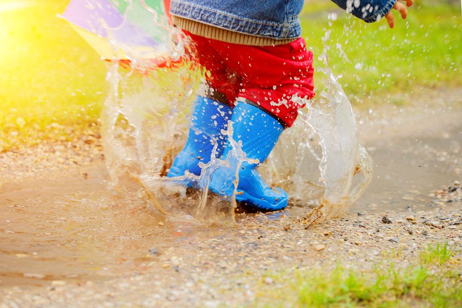 Kindje met blauwe regenlaarsjes springt in regenplas