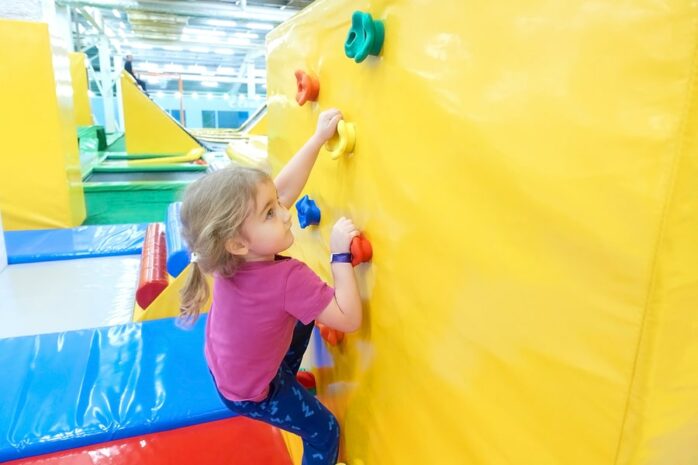 Meisje klimt op kinderklimmuur in binnenspeeltuin