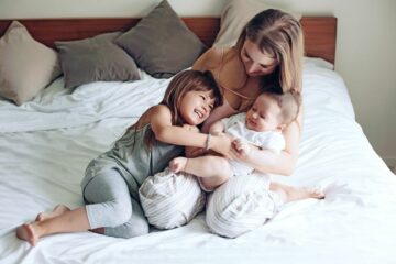 Moeder met haar eerste en tweede kind op bed, verdeelt de aandacht