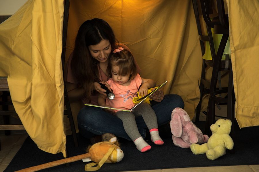 Peuter en moeder zitten samen in zelfgebouwde hut van stoelen en lakens