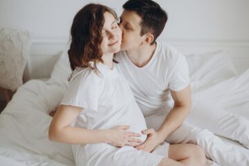 Zwangere vrouw zit ontspannen met partner op bed en voorkomt zo stress tijdens de zwangerschap