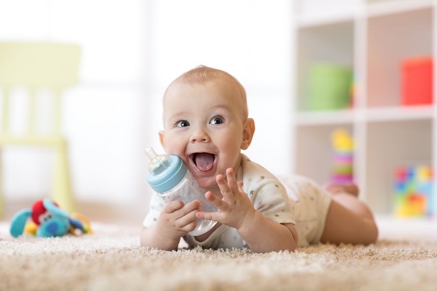 Baby ligt vrolijk op tapijt met een fles
