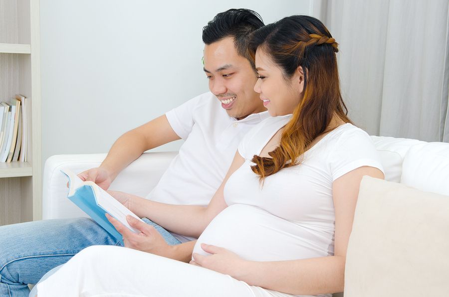 Zwangere vrouw en haar partner lezen boek over zwangerschap in bed