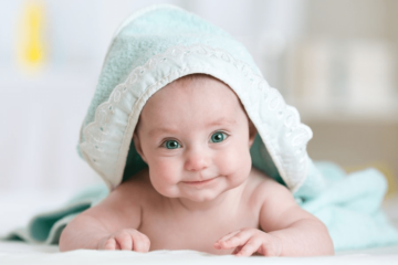 betekenis namen van baby die op zijn buik ligt met badcape aan