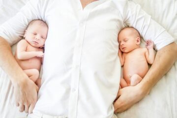 Vader met pasgeboren tweeling in armen op bed