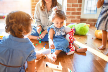 Gastouder speelt met kindjes in haar huis op de vloer