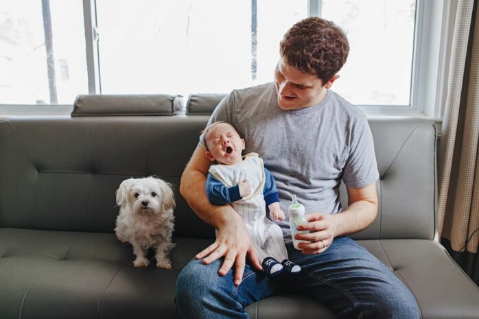 Vader geeft baby de fles met hondje op bank