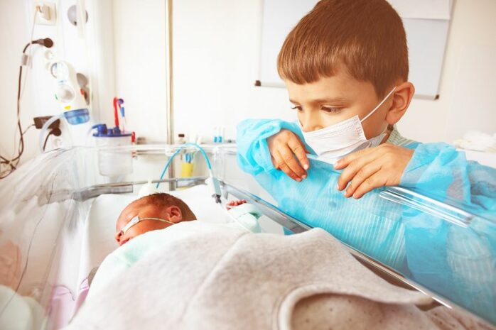 Ouder broertje bekijkt babyzusje in bed op de neonatologie afdeling