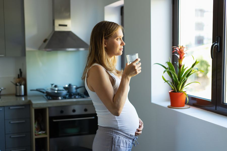 Zwangere vrouw kijkt uit het raam en maakt zich zorgen over het coronavirus tijdens de zwangerschap