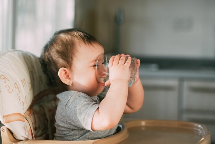 Baby drinkt zelf water uit een glas, wat past in het voedingsschema van een baby van 8 maanden