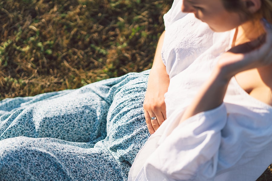 Zwangere vrouw zit in het gras en voelt wat haar fundushoogte is