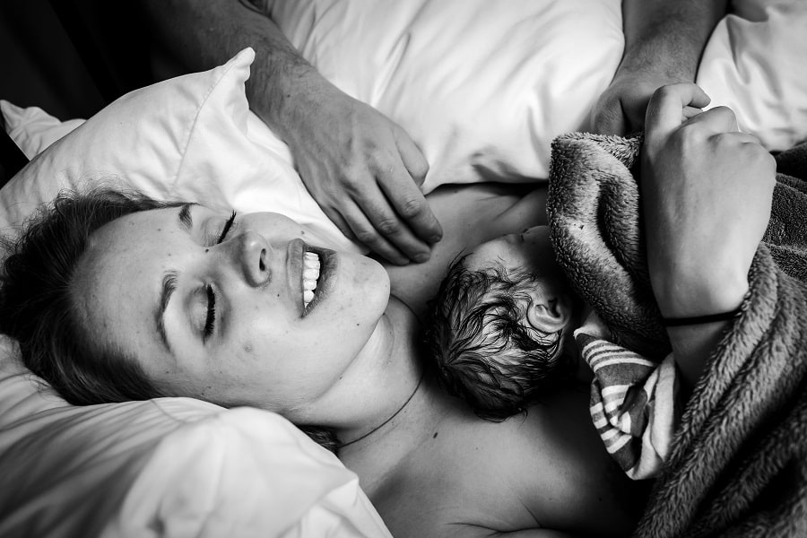 Pas bevallen vrouw ligt voldaan met haar baby op de borst tijdens de nageboorte van de placenta
