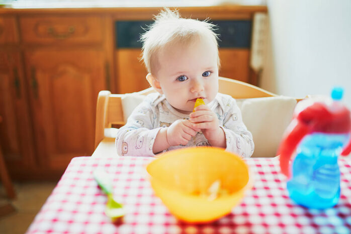 Baby eet Ellas kitchen met lepel in de mond