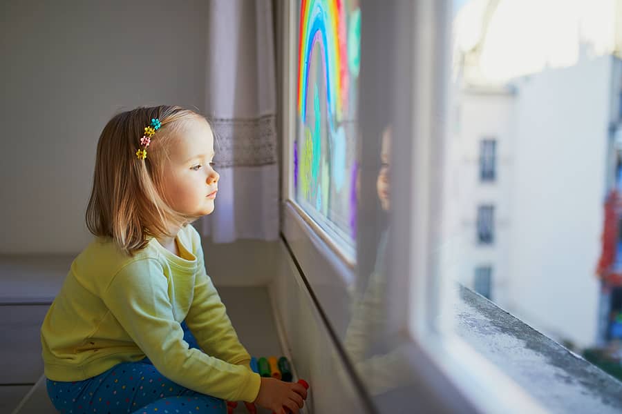 Vergeten kind kijkt hoopvol uit het raam naar regenboog