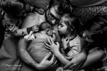 Vader buidelt met pasgeboren baby terwijl dochters toekijken