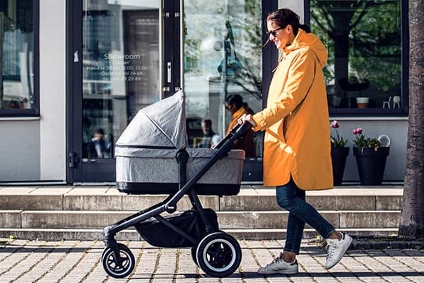 Moeder in regenjas wandelt achter Thule Sleek kinderwagen