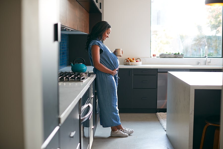 Zwangere vrouw staat in keuken en denkt aan de voedingsstoffen die ze extra nodig heeft.