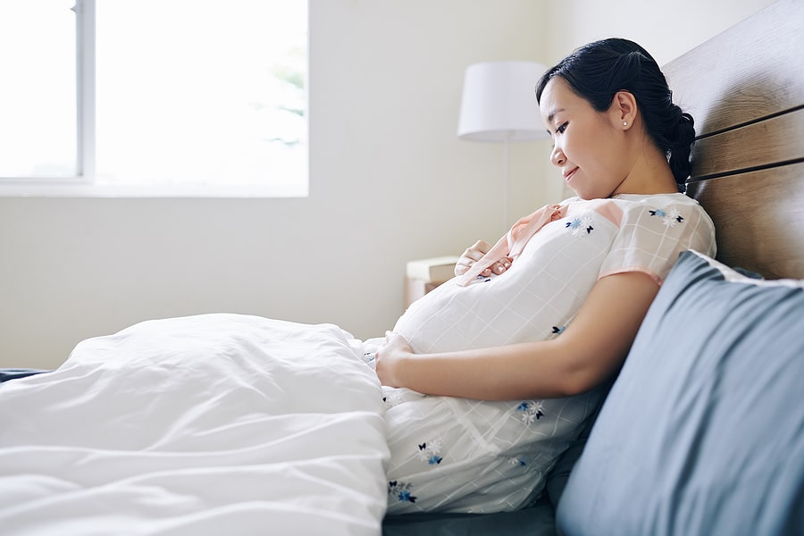 Zwangere vrouw ligt op bed en denkt aan perineum massage