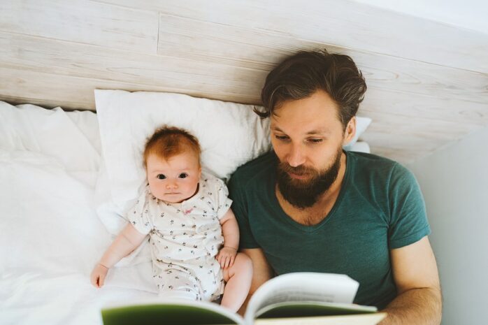 Vader leest op bed boekje met baby van 2 maanden