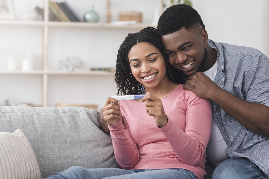 Pärchen sitzt auf der Couch und freut sich über positiven Schwnagerschaftstest