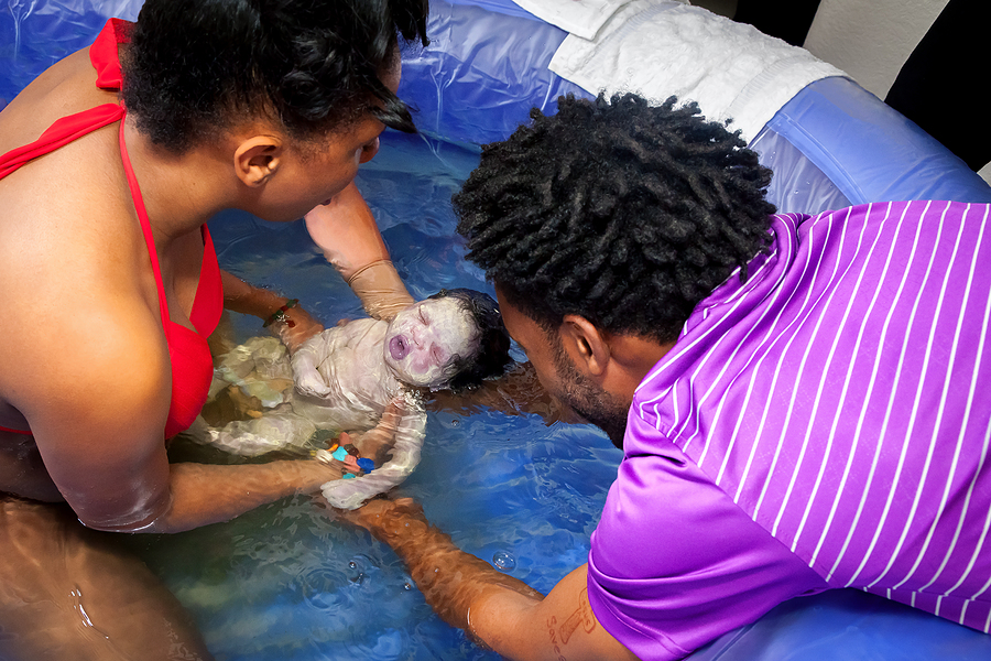 Ein gerade geborenes Baby schwimmt bei der Wassergeburt in die Arme der Eltern.