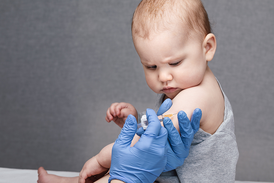 Ein Baby wird geimft und schaut sehr skeptisch auf die Spritze.