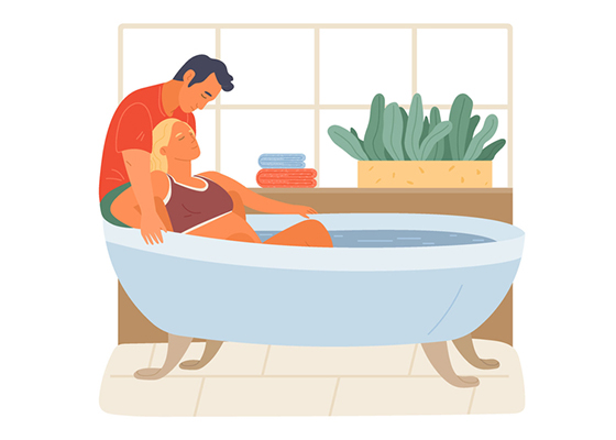 Frau veratmet ihre Wehen in der Wanne. Ihr Partner sitzt hinter ihr.