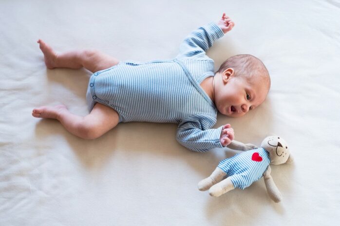 Baby liegt auf dem Boden und hat einen Wickelstrampler an.