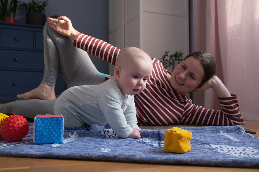 Mama macht Rückbildungsgymnastik auf Spieldecke mit Baby