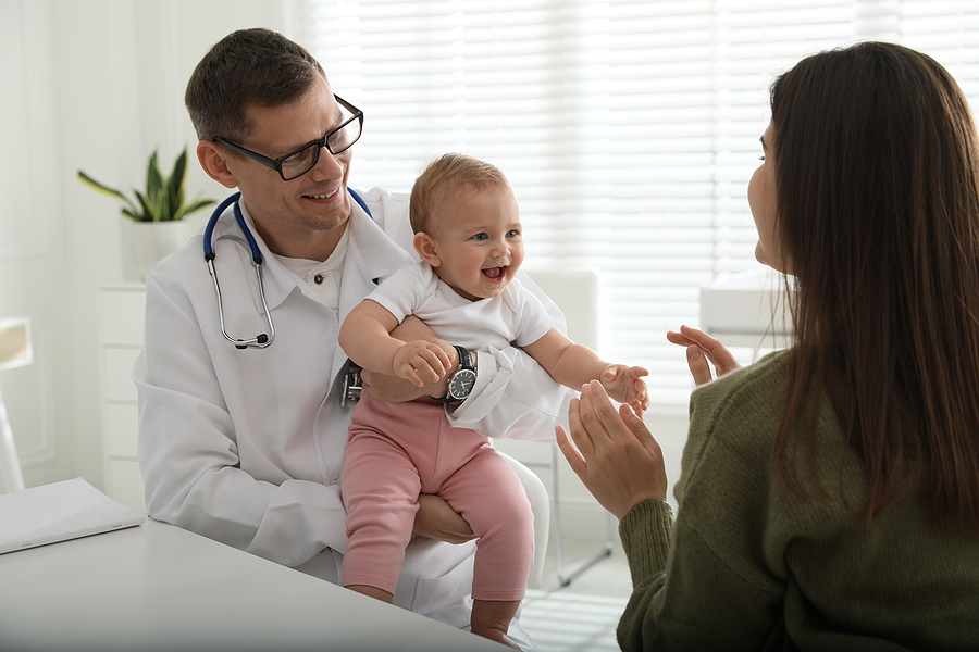Kinderarzt hält ein lachendes Baby während der U6-Untersuchung.
