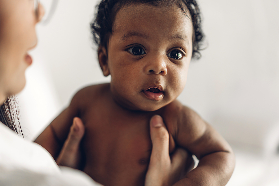 dunkelhäutiges Baby wird von Frau unter den Achseln hochgehoben