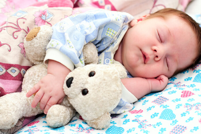 Baby schläft mit Teddy im Arm