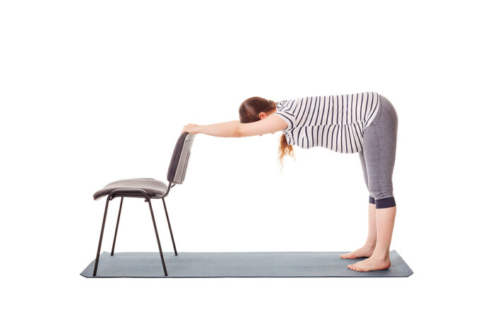 Schwangerschaftsyoga: Schwangere Frau lehnt sich nach vorne, stützt ihre Hände am Stuhl und dehnt den Rücken